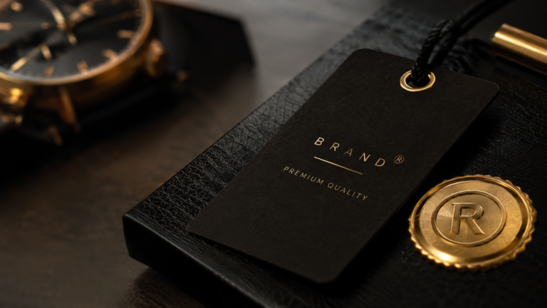 Tag de marca preta com o logotipo “BRAND” e “PREMIUM QUALITY” em destaque sobre uma caixa de textura semelhante a couro, com detalhe dourado ao lado.